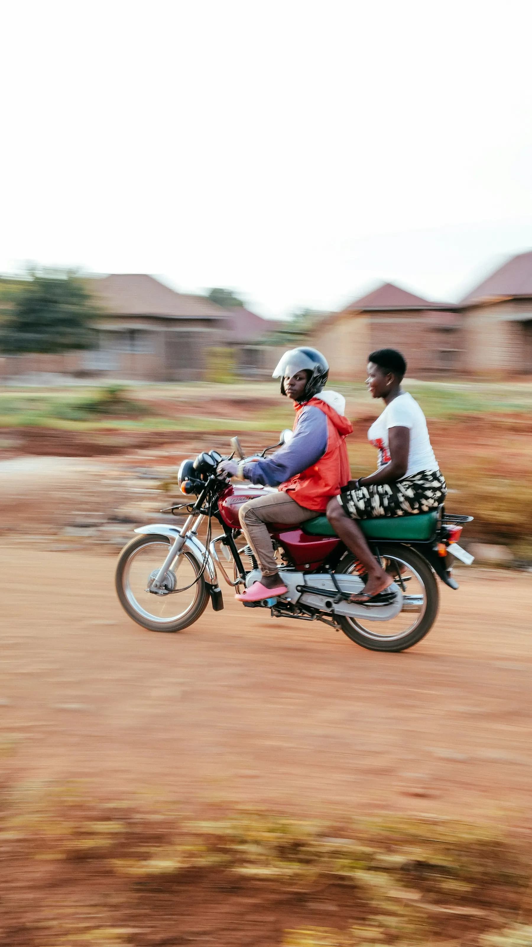 A rider and passenger on a motorbike on a laterite road
